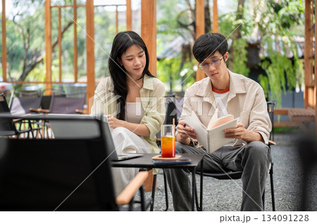 Asian woman is looking or reading a notebook in a man hands while sitting together at folding table. 134091228
