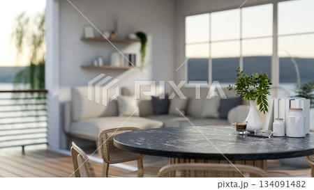 Coffee cup and flower vase on black marble round table in a room with sofas and river view outside. 134091482