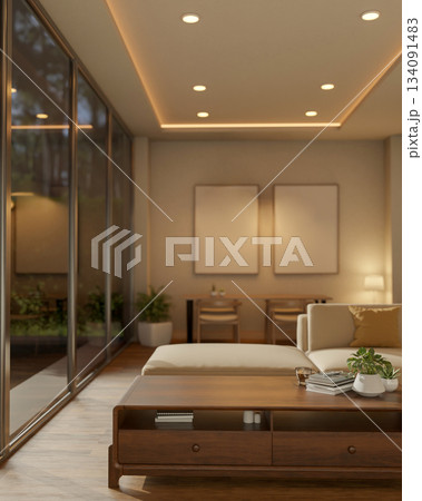 Coffee and books on glass top wooden table next to a white sofa with blank frames hanging on wall. 134091483