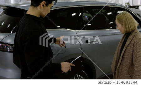 Sales manager showing a new car to a client in the showroom Sales manager showing a new car to a client in the showroom 134091544