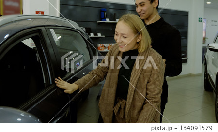 Sales manager pointing out car features to a female client in the showroom 134091579