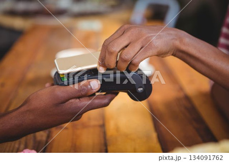 Woman paying bill through smartphone using NFC technology in cafe Woman paying bill through smartphone using NFC technology in cafe 134091762