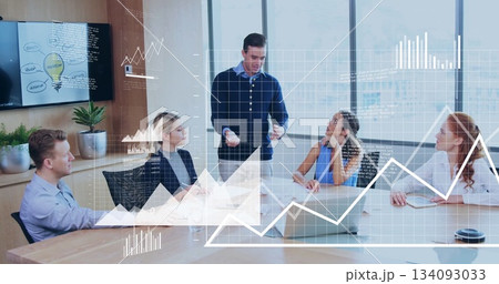 Presenting presenter in navy sweater pointing at display in conference room, with laptop and papers 134093033