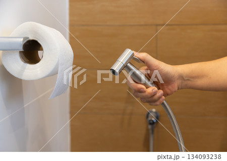 Woman is holding a stainless steel handheld bidet sprayer in bathroom. 134093238