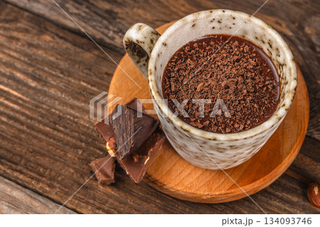Hot chocolate in ceramic cup topped with chocolate shavings on rustic wooden background, cozy winter drink top view Hot chocolate in ceramic cup topped with chocolate shavings on rustic wooden background, cozy winter drink top view 134093746
