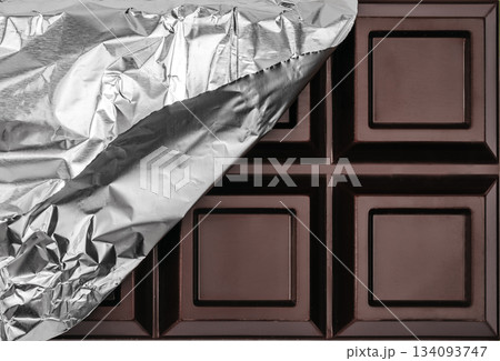 Dark chocolate bar partially unwrapped in silver foil close up background with copy space Dark chocolate bar partially unwrapped in silver foil close up background with copy space 134093747