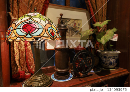 重厚なカーテンとステンドグラスランプ、コーヒーミルが並ぶレトロ喫茶店のインテリア 134093976