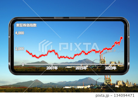 山と工場の風景を切り抜いた構図を壁紙にしたスマホ画面に長期的な株価の推移を表示させているイメージ写真 134094471