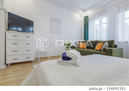 Bright Cozy Room with Green Sofa and Fresh Towels on Bed 134095381