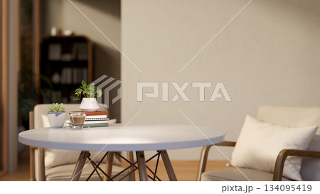 A glass of coffee and books aside potted plants on white round table with chairs in a living room. A glass of coffee and books aside potted plants on white round table with chairs in a living room. 134095419