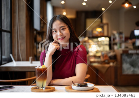 Young asian woman resting head on hand sitting with orange coffee aside cake on table in the cafe. Young asian woman resting head on hand sitting with orange coffee aside cake on table in the cafe. 134095463