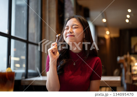 Young asian woman closing eyes smiling while holding raising a spoon enjoy eating at table in cafe. 134095470