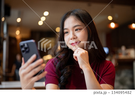 Close up pretty asian woman holding looking at smartphone resting head on hand while sitting in cafe Close up pretty asian woman holding looking at smartphone resting head on hand while sitting in cafe 134095482