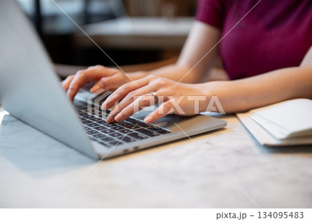 Close up of woman's hand wearings ring working or typing on laptop sitting at marble table in a cafe Close up of woman's hand wearings ring working or typing on laptop sitting at marble table in a cafe 134095483