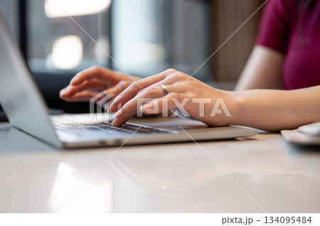 Close up of woman's hand wearings ring working or typing on laptop while sitting at table in a cafe. Close up of woman's hand wearings ring working or typing on laptop while sitting at table in a cafe. 134095484