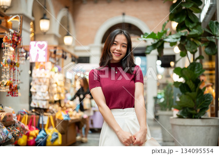 Asian woman tourist customer standing beside a souvenir cart in an indoor market or shopping mall. 134095554