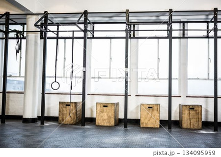 Black metal pull-up rig is spanning gym, featuring gymnastic rings, climbing rope, wooden boxes Black metal pull-up rig is spanning gym, featuring gymnastic rings, climbing rope, wooden boxes 134095959