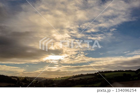 Sunlight is filtering through dramatic sky over rolling green hills and farmland in flat design 134096254