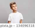Stylish young boy with trendy modern haircut in studio, wearing white T-shirt and looking aside, isolated on gray background in fashion portrait 134096318