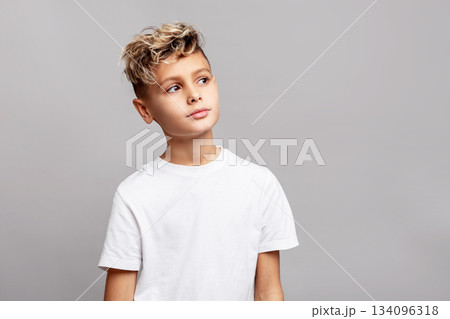 Stylish young boy with trendy modern haircut in studio, wearing white T-shirt and looking aside, isolated on gray background in fashion portrait Stylish young boy with trendy modern haircut in studio, wearing white T-shirt and looking aside, isolated on gray background in fashion portrait 134096318