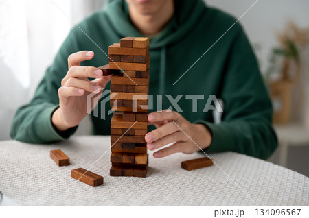 Close up man's hands taking out a piece of wooden blocks in tower building game while playing alone. Close up man's hands taking out a piece of wooden blocks in tower building game while playing alone. 134096567