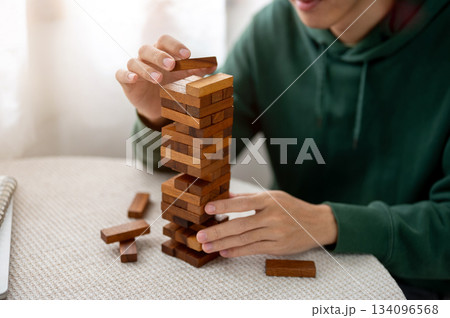Close up a man's hand putting a piece on top of wooden block toy tower playing alone on round table Close up a man's hand putting a piece on top of wooden block toy tower playing alone on round table 134096568