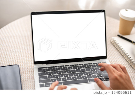 Hands typing on white screen laptop aside notebook and coffee on round table in cafe or living room. 134096611