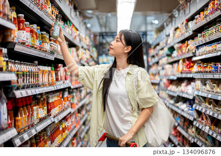 Chiang mai, Thailand - September 16th, 2025: A woman shopping taking product from supermarket shelf. Chiang mai, Thailand - September 16th, 2025: A woman shopping taking product from supermarket shelf. 134096876