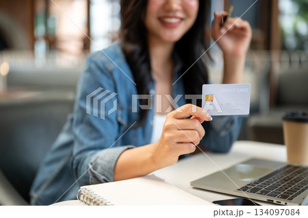 Close up blurred woman holding or showing credit card sitting with laptop and notebook at cafe table Close up blurred woman holding or showing credit card sitting with laptop and notebook at cafe table 134097084