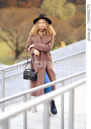 Woman in brown coat stands on stairs in park during autumn Woman in brown coat stands on stairs in park during autumn 134098279