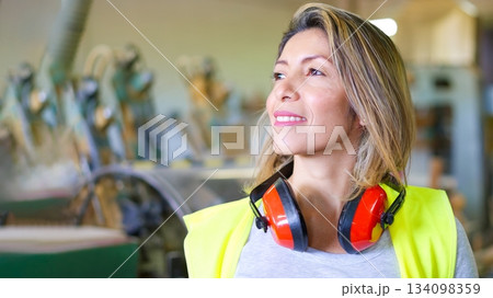 Woman industrial worker wearing safety vest and earmuffs 134098359