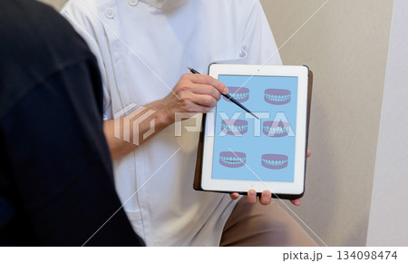 歯科医がタブレットの歯列図を用いて噛み合わせや治療方針を説明する様子 歯科医がタブレットの歯列図を用いて噛み合わせや治療方針を説明する様子 134098474