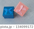 Two small boxes with ribbons are placed on a shiny surface. One box is blue and the other is pink. These boxes are ready for gifting during a party or event. 134099172
