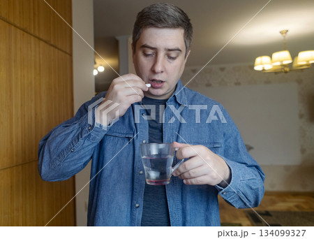 Man taking dietary supplements at home, pouring pills from a bottle and drinking with water. Concept of daily vitamins, health care and wellness routine. Man taking dietary supplements at home, pouring pills from a bottle and drinking with water. Concept of daily vitamins, health care and wellness routine. 134099327