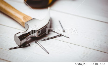 Flat design claw hammer and scattered nails are resting on painted white wooden plank surface 134101483