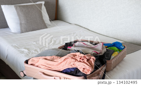Traveler packing an open suitcase on the bed, organizing essentials for an upcoming journey 134102495