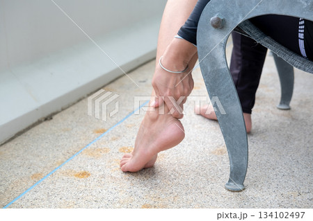Young Asian woman massaging her ankle on balcony chair, calming wellness moment with fresh air 134102497