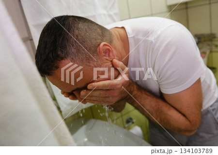 Man washing face, hygiene and skincare with water, basin and grooming during morning routine. Male person in bathroom, cleaning skin with hands and cleanliness, wellness and self care at home 134103789