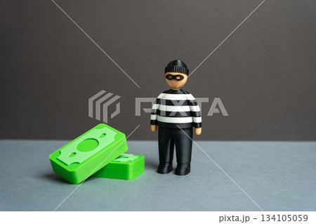 Thief figure stands next to a stack of money. Symbolizing financial crime, corruption, theft, fraud, or illegal income in business and finance concepts. 134105059