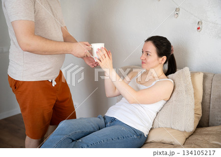 A man serves tea to a woman sitting on a bed. Concept of caring for a sick relative, support A man serves tea to a woman sitting on a bed. Concept of caring for a sick relative, support 134105217