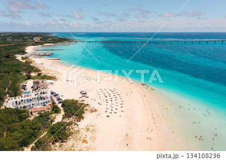 Tourists enjoy a sunny day at a tropical beach with clear blue waters and a long bridge 134108236