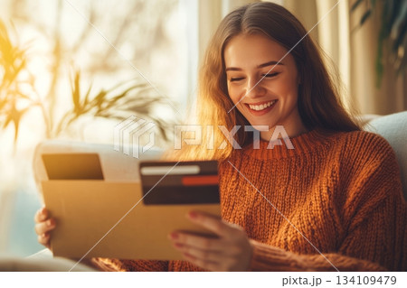 Woman sitting on couch holding credit card in modern living room setting 134109479