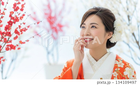 オレンジ色の振袖を着て微笑む日本人女性と紅白の梅の飾り オレンジ色の振袖を着て微笑む日本人女性と紅白の梅の飾り 134109497