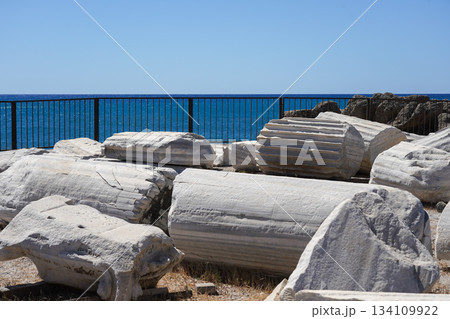 Ancient Ruins by the Sea: Weathered Columns and Fragments Along the Coastline against a Clear Blue Sky 134109922
