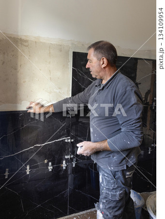 Craftsman placing tile spacers during tiling a wall, closeup. Construction or rennovation of a house 134109954