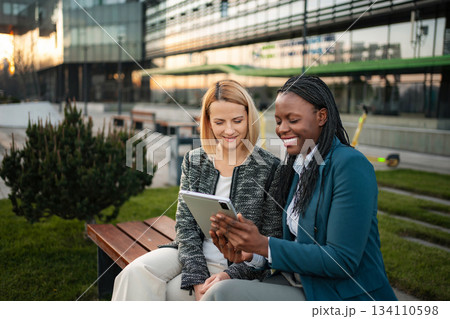 Diverse businesswomen collaborating outdoors with digital tablet Diverse businesswomen collaborating outdoors with digital tablet 134110598