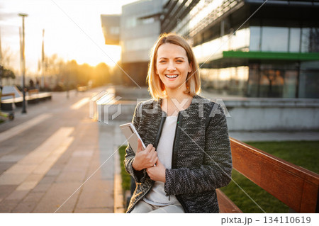 Businesswoman smiling holding tablet in urban sunset at modern office 134110619