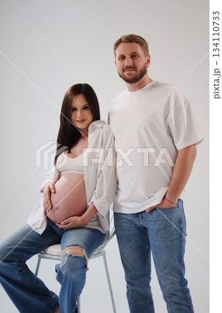Expecting parents pose together in a cozy studio setting Expecting parents pose together in a cozy studio setting 134110733
