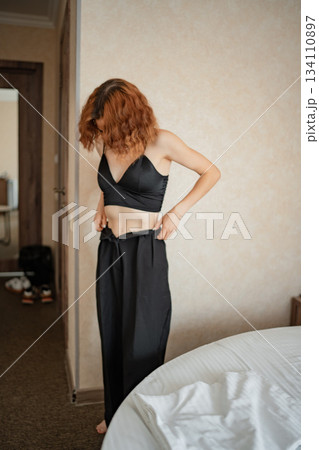 Woman adjusts her black pants in a hotel room before going out 134110897