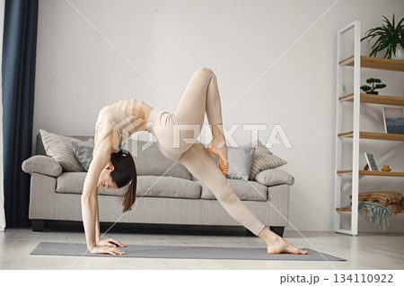Attractive young woman doing yoga stretching at home. Brunette woman wearing beige leggins and top. Self-isolation is beneficial, entertainment and education on the Internet. Attractive young woman doing yoga stretching at home. Brunette woman wearing beige leggins and top. Self-isolation is beneficial, entertainment and education on the Internet. 134110922